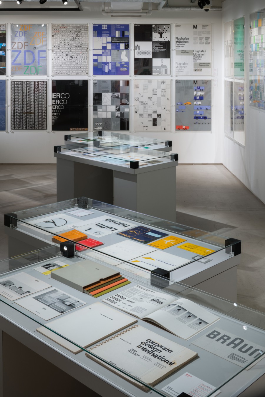 Glasvitrine mit Ausstellungsdokumenten zu Laufthansa-, Braun, ZDF- und ERCO-Erscheinungsbild an weißer Wand