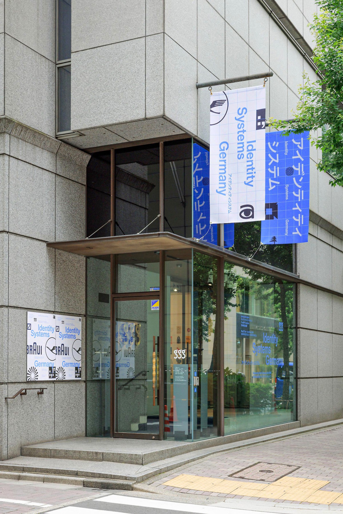 Außenansicht der ddd gallery in Kyoto, Japan mit Ausstellungsfahnen und Plakaten der „Identity Systems Germany“-Ausstellung in englisch und japanisch