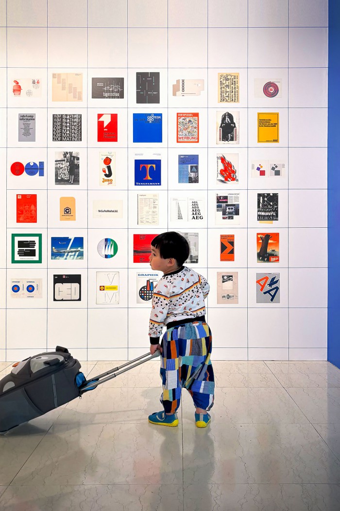 Kind mit Trolley vor der großformatigen Logowand der Ausstellung mit historischen deutschen Corporate-Design-Marken wie ZDF, SPD, Lufthansa, AEG und Tengelmann