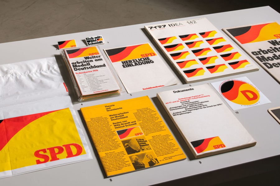 Ausstellungstisch mit dem Erscheinungsbild der SPD von Helmut Schmid, darunter Wahlkampfmaterial „Weiter arbeiten am Modell Deutschland" (1976) und ein Beitrag im japanischen Designmagazin IDEA