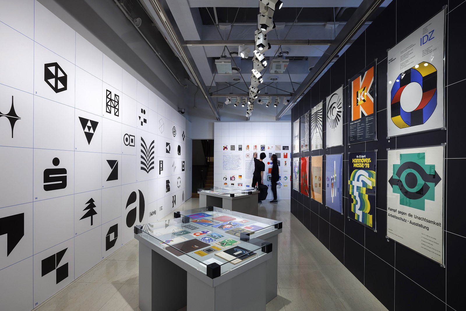 Ansicht eines Ausstellungsraums mit großformatiger Logo-Wand, Glasvitrinen mit Exponaten und historischen Plakaten beispielsweise von der Hannover Messe und IDZ