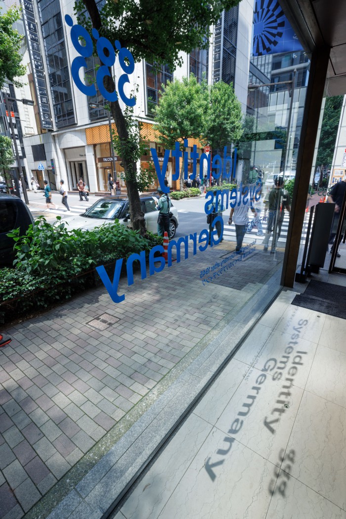 Blick aus der ggg Gallery in Tokio durch die Fensterscheibe mit blauer Beschriftung „Identity Systems Germany – Rebranding West Germany after 1945" auf die Straße im Ginza-Viertel