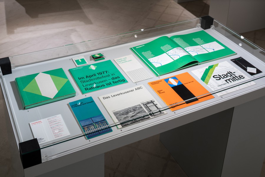 Glasvitrine mit grünen Broschüren und Druckerzeugnissen zu Stadtidentitätsprojekt Leverkusen der 1970er Jahre; Designer: Rolf Müller