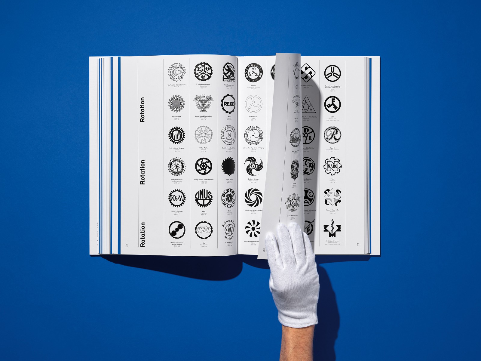 Hand in weißem Handschuh hält aufgeschlagene Buchseite mit Übersicht an Firmenlogos und Markenzeichen in der Kategorie Rotation