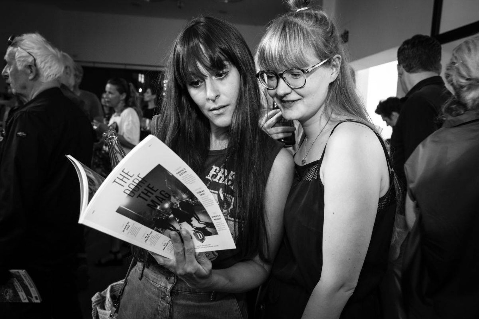 Schwarzweißaufnahme zweier Frauen auf der THE DORF THE MAG Release Party No. 1 Veranstaltung, eine hält ein Exemplar des Magazins